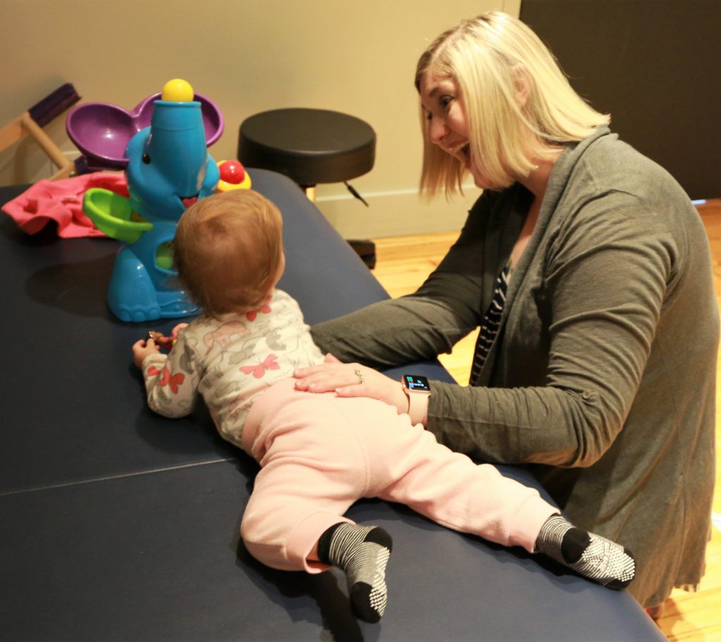 Smiling physical therapist assisting a baby in crawling.