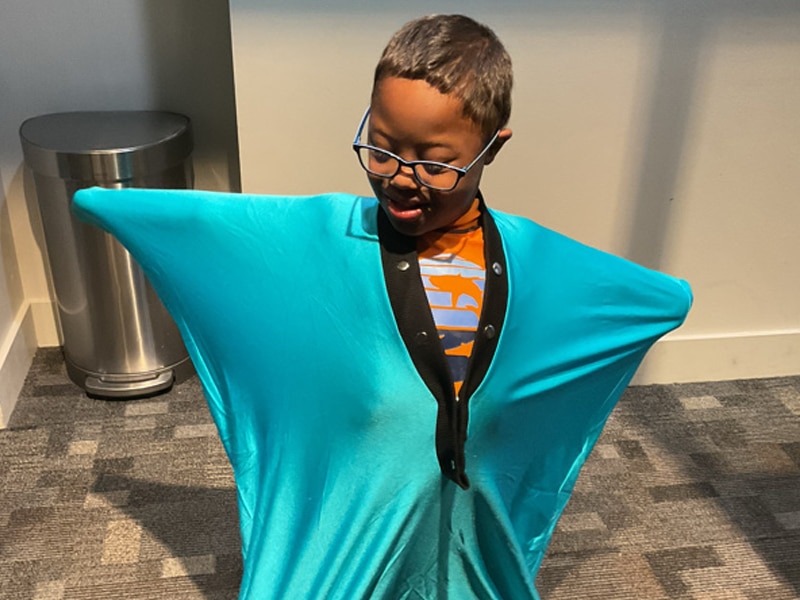 Child at Eyas Landing wearing turquoise body sock and standing with his arms outstretched