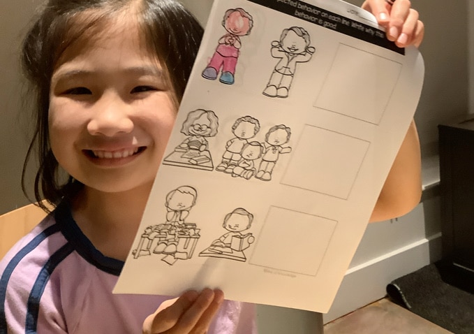 child smiling and holding up worksheet