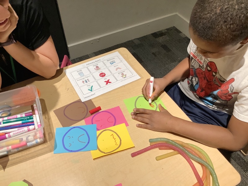 Child drawing emotion faces on a worksheet while sitting at a table at Eyas Landing