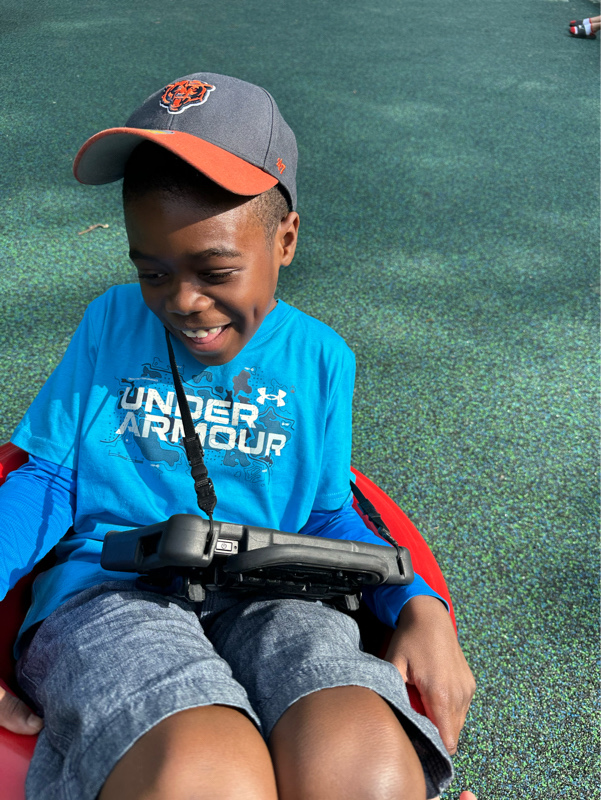 child smiling in wagon with his AAC communication device at Eyas Landing chicago