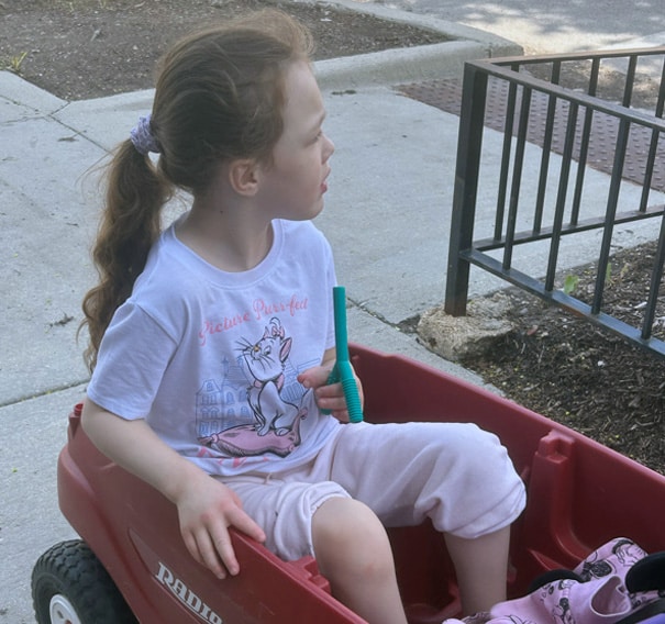 Child sitting in wagon holding chewelry shaped like a y