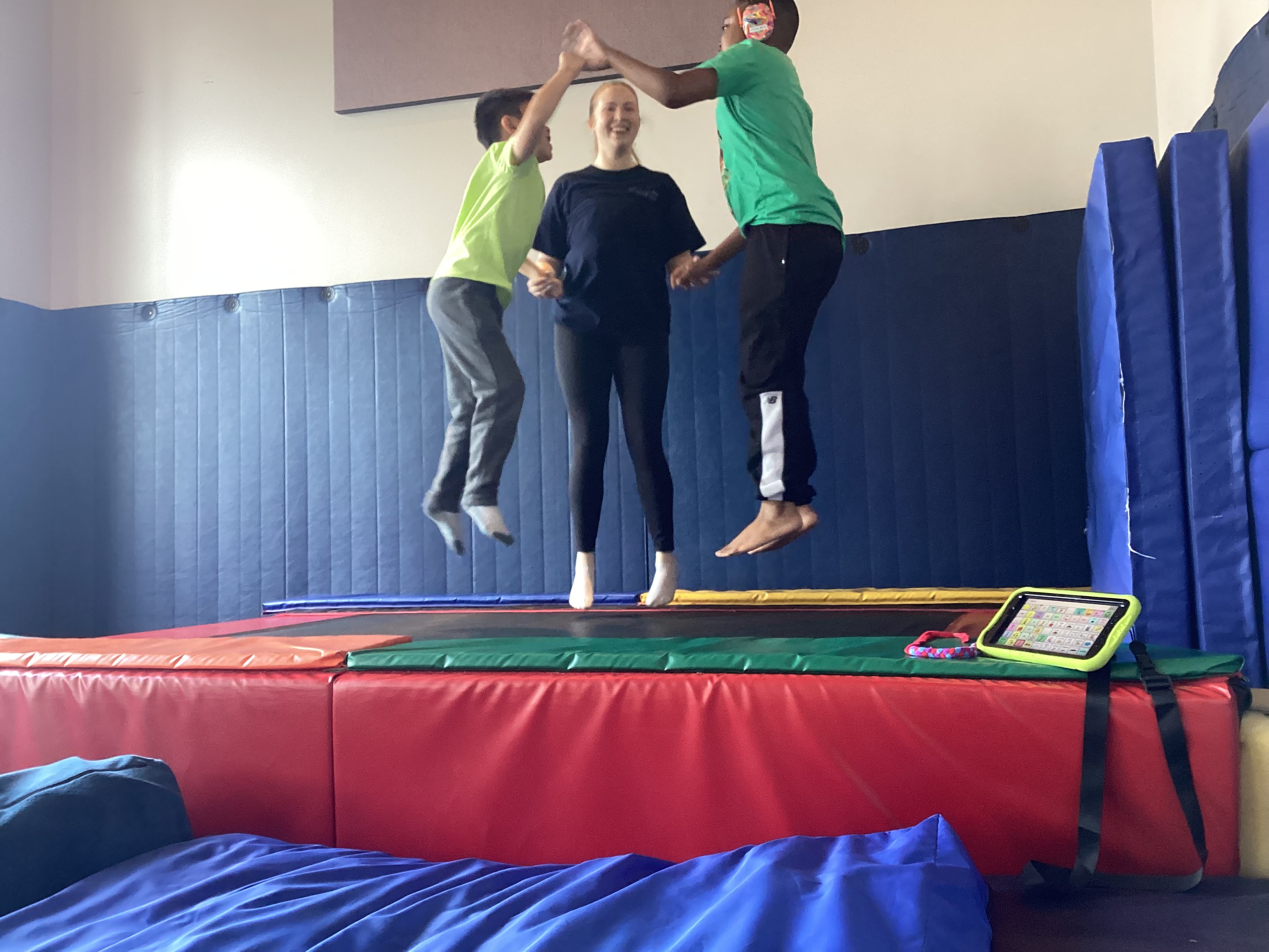 Two children and a therapist jumping on a trampoline in a therapy gym