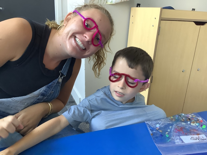 A child sitting with his therapist wearing silly glasses. A child sitting with his therapist wearing silly glasses.