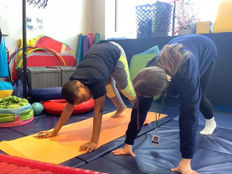 a child and his therapist doing yoga in the eyas landing west loop sensory gym.